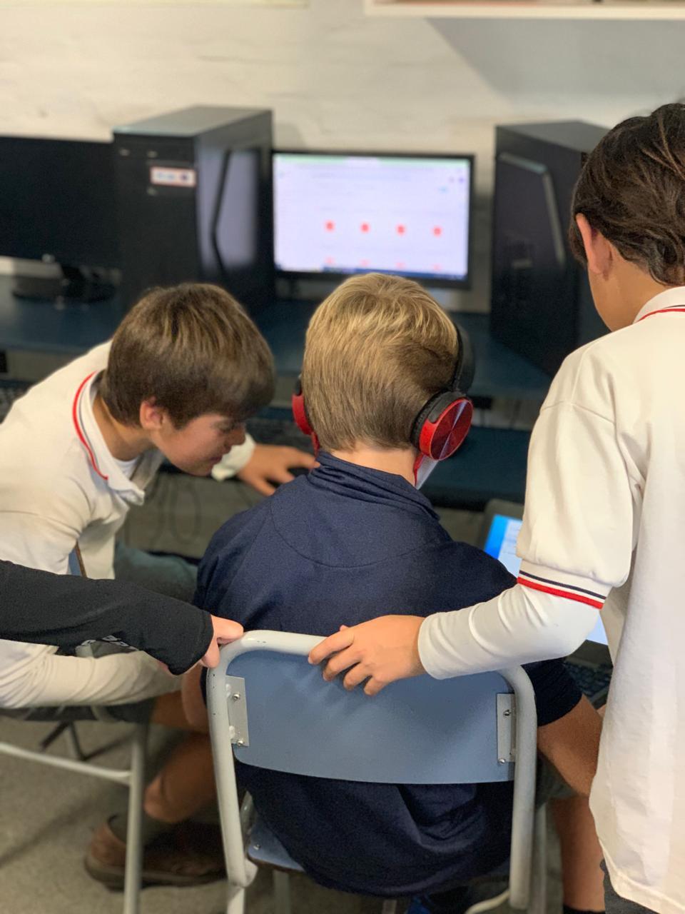 Fotografía de 3 estudiantes viendo una computadora y uno de ellos con auriculares