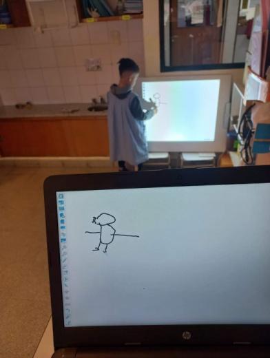 Un estudiante dibujando en la pizarra interactiva y de frente se ve ese dibujo en una computadora
