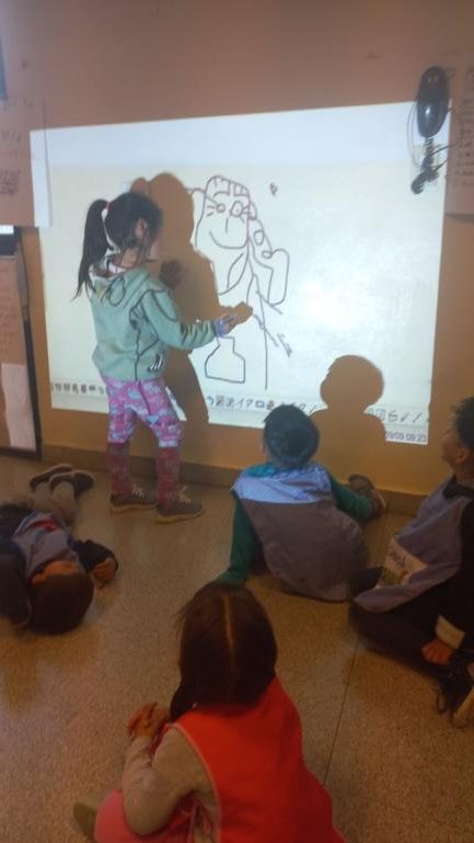 Nena interactuando con un dibujo en la pizarra que se refleja en una pared
