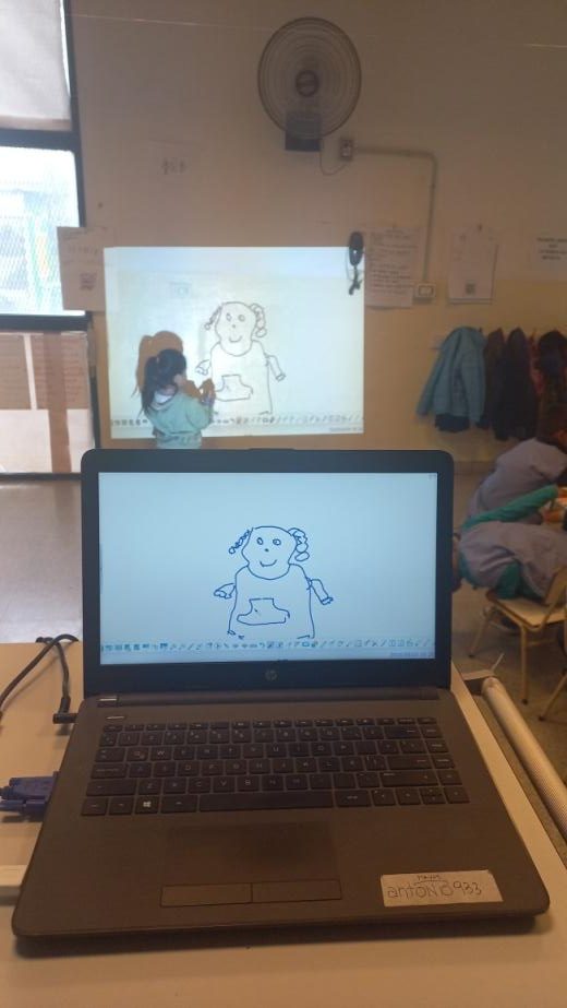 Un estudiante dibujando en la pizarra interactiva y de frente se ve ese dibujo en una computadora