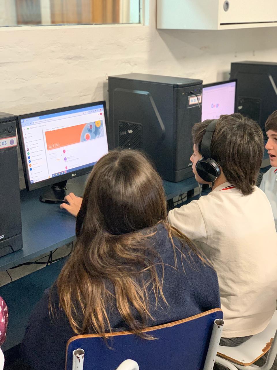 Fotografía de 3 estudiantes viendo una computadora y uno de ellos con auriculares