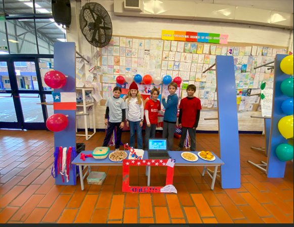 Fotografía de 5 niños con la representación de un stand de Chile, con comidas y bandera del país